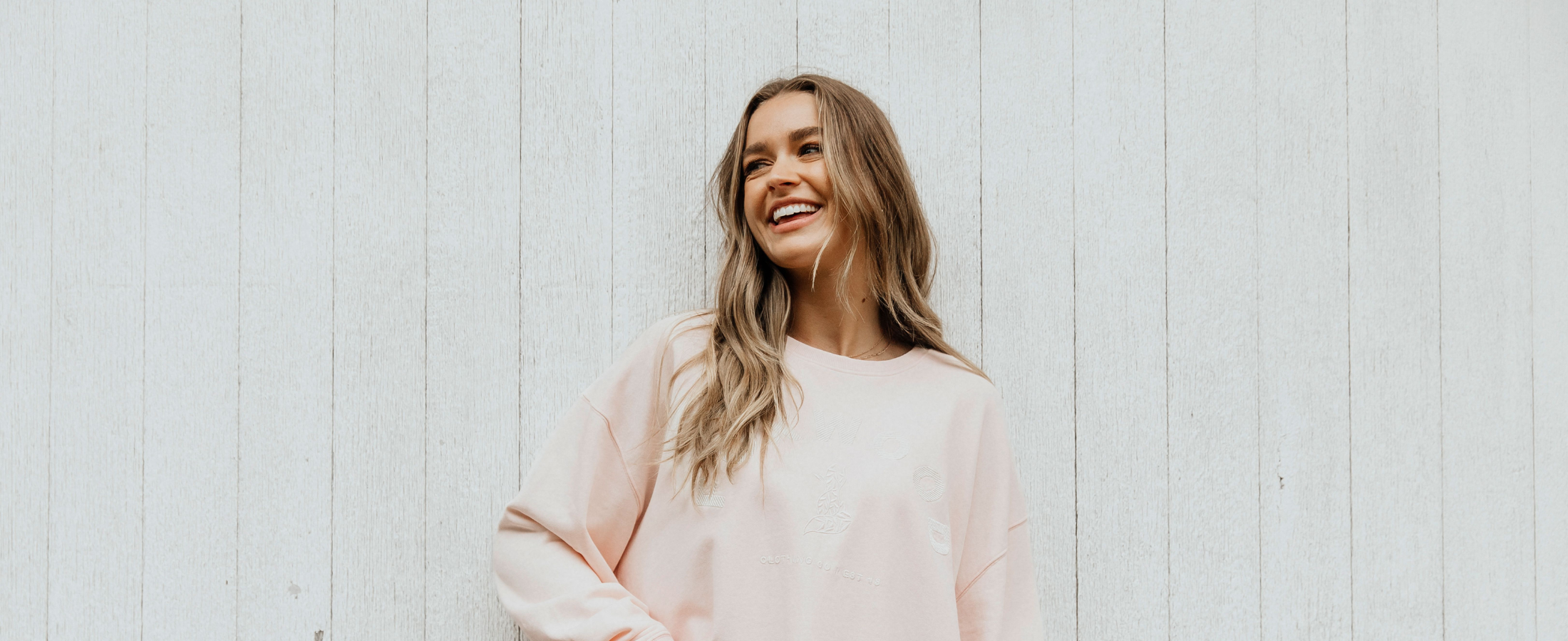 a female standing in front of a white fence smiling