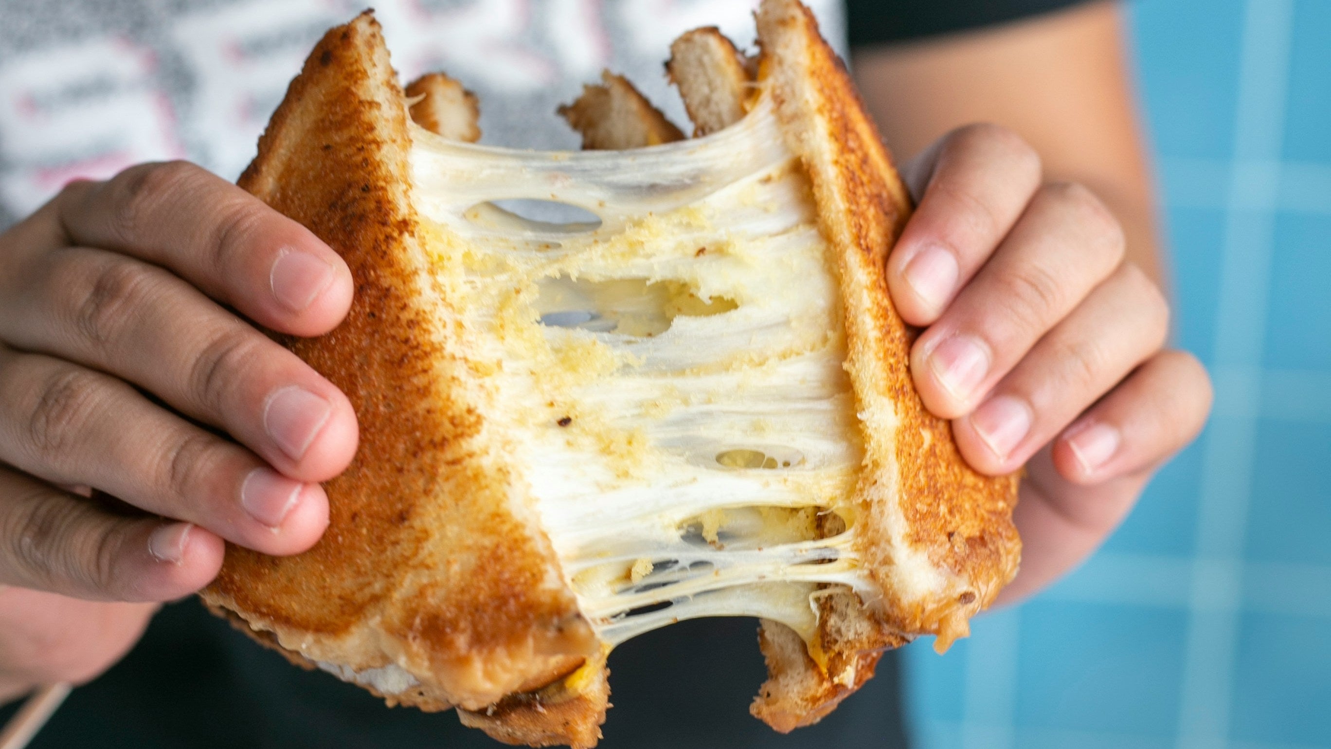 Person holding a grilled cheese sandwich with stretchy cheese, blurred background